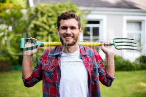 Smiling man carrying rake while standing in yard