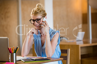 Graphic designer in office sitting at desk and talking on mobile