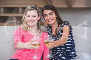 Two beautiful women showing their glass of wine in the living ro