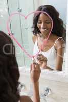 Beautiful young woman drawing big heart on mirror