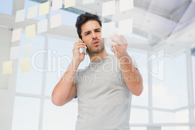 Man looking at a sticky notes while talking on phone Man looking at a sticky notes while talking on phone