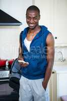 Man with gym bag holding a mobile phone in kitchen