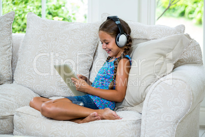 Girl using digital tablet while listening music on sofa