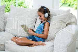 Girl using digital tablet while listening music on sofa