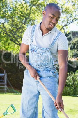 Young man in dungarees raking the garden