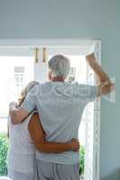Senior couple looking through window at home