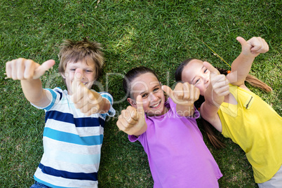 Portrait of happy children showing thumbs up while lying on the