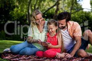 Happy parents with daughter looking at mobile phone in yard