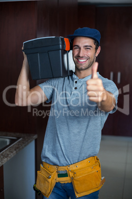 Smiling man carrying toolbox while showing thumbs up