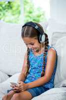 Girl listening music while using mobile phone on sofa