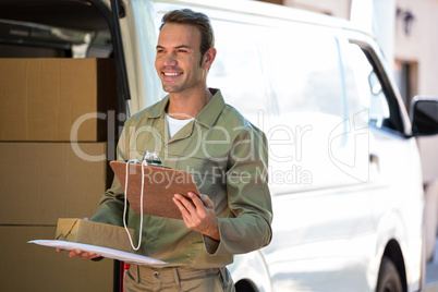 Happy delivery man holding cardboard box and clipboard