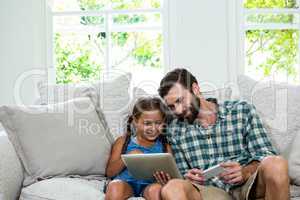 Happy girl showing digital tablet to father on sofa