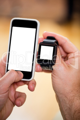 Mans hand holding a smart watch and a mobile phone