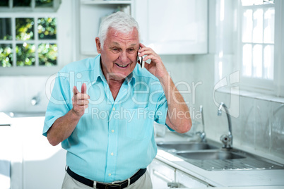 Senior man talking on phone in kitchen