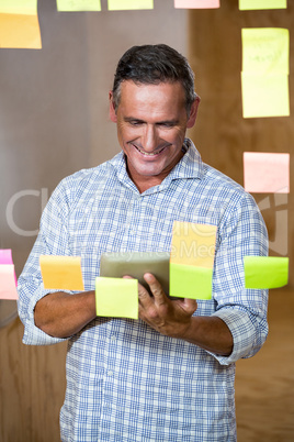 Man looking at digital tablet and sticky notes on window