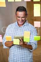 Man looking at digital tablet and sticky notes on window