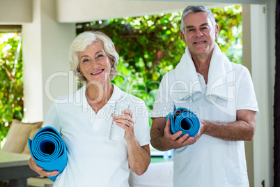Happy senior couple holding exercise mats