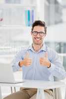 Businessman showing thumbs up while using laptop