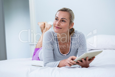 Smiling woman with digital tablet while lying on bed