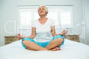 Old woman performing yoga on bed