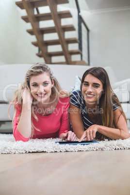 Two beautiful women lying on rug and using digital tablet