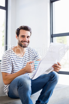 Portrait of happy man on steps holding cup of coffee and reading