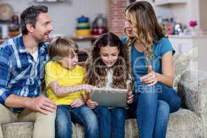 Parents and kids sitting on sofa and using a digital tablet