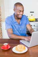 Young man having breakfast and using laptop