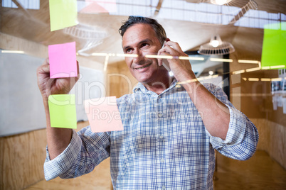 Man writing on sticky notes while talking on phone