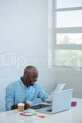 Graphic designer reading a document with laptop on table