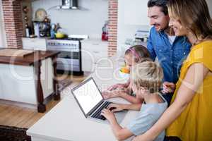 Parents and kids using laptop in kitchen