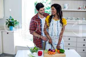Man embracing woman while chopping vegetables