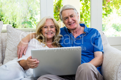 Smiling senior couple holding tablet sitting at home