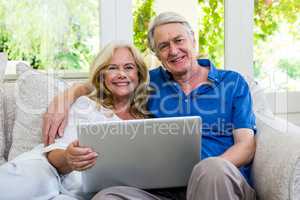 Smiling senior couple holding tablet sitting at home