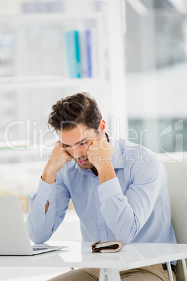 Tensed businessman sitting at table with laptop