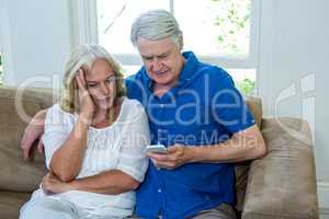Senior couple using mobile phone while sitting on sofa