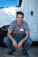 Smiling delivery man crouching by van