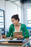 Woman using laptop and holding digital tablet