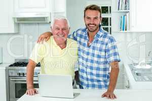 Man standing with father by laptop at table in kitchen