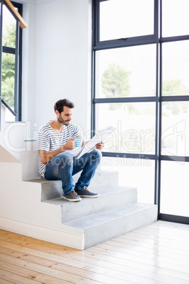 Man on steps having cup of coffee while reading newspaper