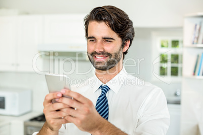 Smiling businessman using cellphone in kitchen