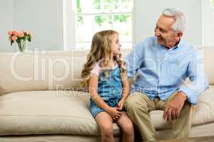 Happy grandfather and girl sitting on sofa