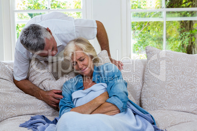 Senior man talking to ill wife resting on sofa