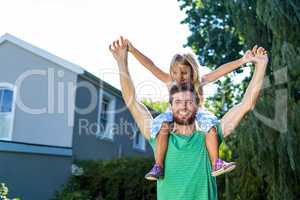 Portrait of father carry daughter on shoulders in yard