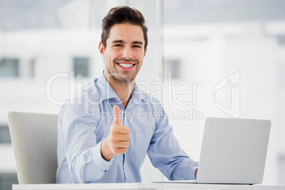 Businessman showing thumbs up while using laptop Businessman showing thumbs up while using laptop