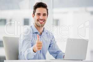 Businessman showing thumbs up while using laptop