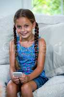 Smiling girl using mobile phone while sitting on sofa
