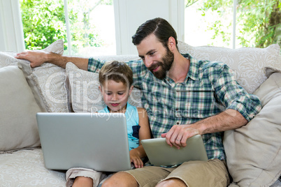 Smiling father sitting by son with laptop on sofa