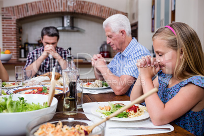 Multi-generation family praying before having meal