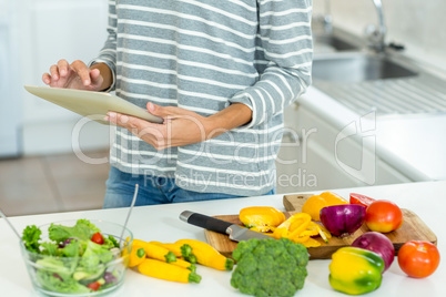 Woman using digital tablet by vegetables in kitchen